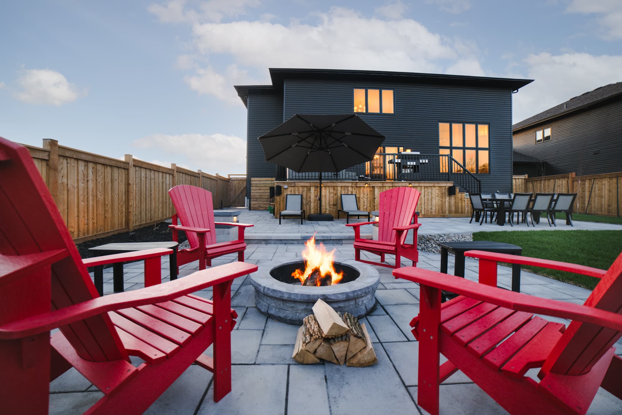 Marcus’s House at dusk with a fire pit and red Muskoka chairs